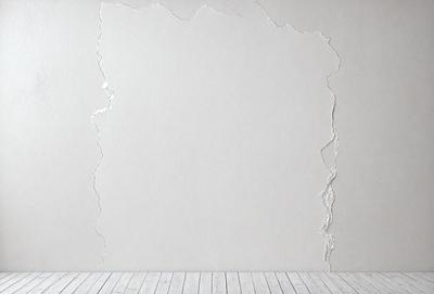 The primary subject of the image is a white wall with a large hole in it. The setting is a room with a wooden floor. The visual style is a photo, and the colors and mood are predominantly white, giving the image a clean and minimalist appearance.