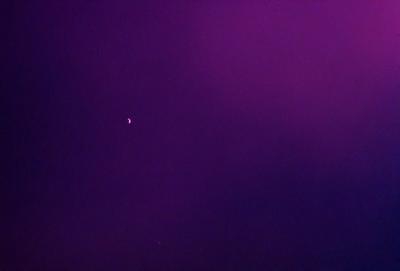 The primary subject of the image is a purple sky with a few stars visible. The setting is a dark, cloudy night with a purple hue. The visual style is a photo, capturing the night sky with the stars and the purple hue. The colors and mood of the image are predominantly purple, creating a serene and peaceful atmosphere.