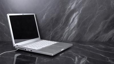 The primary subject of the image is a laptop computer. It is placed on a black marble countertop, which serves as the setting and background. The visual style of the image is a photo, capturing the laptop in its natural environment. The colors and mood of the image are predominantly black and white, giving it a sleek and modern appearance.