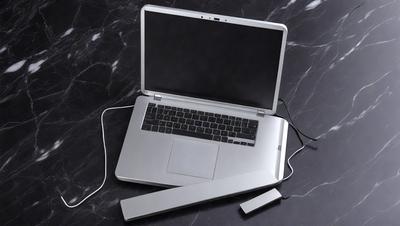 The primary subject of the image is a laptop computer. The laptop is open and sitting on a black marble surface. The setting appears to be a workspace or a home office. The visual style of the image is a photo, capturing the laptop and its surroundings. The colors in the image are predominantly black and grey, giving the scene a professional and sophisticated atmosphere.