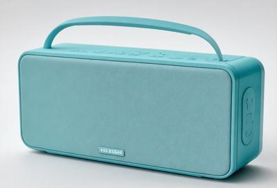 The primary subject of the image is a blue speaker, which is the main object in the scene. The speaker is placed on a white surface, which serves as the background. The visual style of the image is a photo, capturing the speaker in detail. The dominant colors in the image are blue and white, creating a clean and modern atmosphere.
