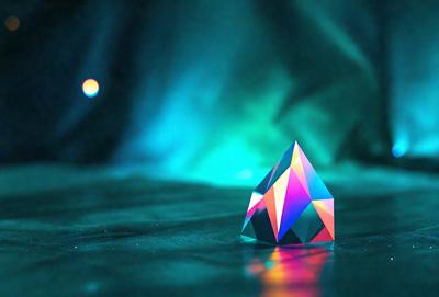 The primary subject of the image is a colorful, geometric shape, possibly a crystal or a piece of art, sitting on a dark surface. The setting appears to be a dark room or a space with a blue background. The visual style of the image is a combination of photo and digital art, creating a unique and intriguing appearance. The colors and mood of the image are predominantly dark and moody, with the geometric shape standing out as the focal point.