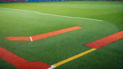 The image features a green field with a yellow line painted on it. The field appears to be a soccer field, and the yellow line is likely a boundary marker. The primary subject of the image is the soccer field, and the setting is an outdoor sports field. The visual style of the image is a photo, and the colors and mood are vibrant and energetic, typical of a sports field.