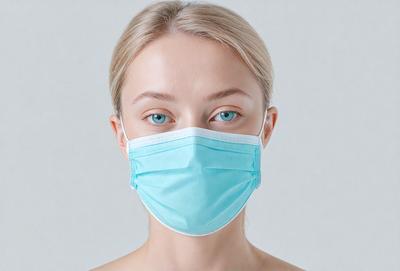 The primary subject of the image is a woman wearing a blue face mask. The setting is a white background, which provides a clean and minimalistic look. The visual style is a close-up of the woman's face, emphasizing the mask and her features. The colors in the image are predominantly blue, which gives the image a calm and professional atmosphere.