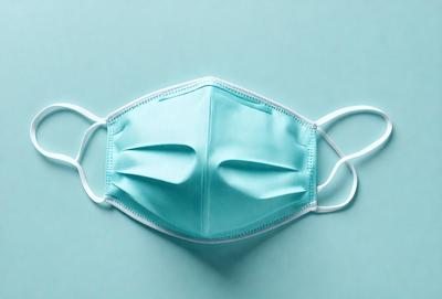The primary subject of the image is a blue face mask. The mask is placed on a blue surface, which serves as the background. The visual style of the image is a close-up of the face mask, emphasizing its details. The dominant colors in the image are blue and white, creating a calm and soothing atmosphere.
