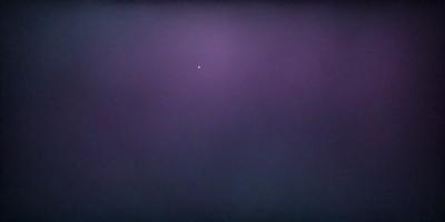 The primary subject of the image is a single star in the night sky. The setting is a dark, cloudy night with a purple hue. The visual style is a photo of the night sky, capturing the star and its surroundings. The colors and mood of the image are predominantly purple, creating a serene and peaceful atmosphere.