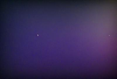 The primary subject of the image is a moon, which is visible in the sky. The setting is a dark, cloudy night with a purple hue. The visual style is a photo, capturing the moon in its natural environment. The colors and mood of the image are predominantly purple, creating a serene and atmospheric scene.