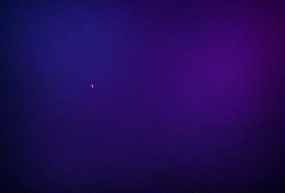 The primary subject of the image is a moon, which is visible in the dark sky. The setting is a purple background, which adds a unique and artistic touch to the scene. The visual style is a combination of a photo and digital art, creating a striking and visually appealing image. The colors and mood of the image are predominantly dark and moody, with the purple background providing a contrasting and eye-catching element.
