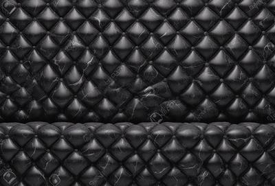 The primary subject of the image is a black leather couch with a patterned design. The setting is a room with a black and white marble wall, which serves as the background. The visual style is a close-up of the couch, showcasing its unique pattern. The colors and mood of the image are predominantly black and white, giving it a modern and sophisticated appearance.
