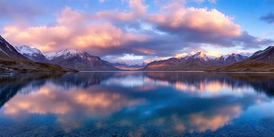 The primary subject of the image is a large body of water, which appears to be a lake. The setting is a mountainous area, with snow-capped mountains visible in the background. The visual style of the image is a photo, capturing the beauty of the natural landscape. The colors and mood of the image are serene and tranquil, with the blue water and the majestic mountains creating a peaceful atmosphere.