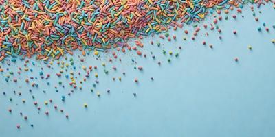 The primary subject of the image is a close-up of a colorful candy display. The setting is a blue surface, which serves as the background. The visual style is a combination of photo and digital art, creating a vibrant and lively atmosphere. The dominant colors are blue, pink, yellow, and green, which contribute to the overall cheerful and playful mood of the scene.