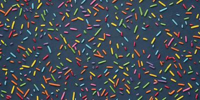 The primary subject of the image is a close-up of a colorful, patterned surface, likely a table or a wall, with a variety of colors and shapes. The setting appears to be a room with a blue background. The visual style of the image is a combination of photo and digital art, creating a vibrant and lively atmosphere. The dominant colors in the image are pink, yellow, green, and blue, which contribute to the overall cheerful and lively mood.