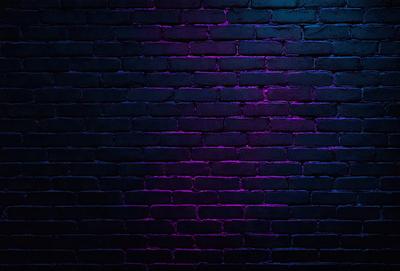 The primary subject of the image is a brick wall. The setting is a dark room with a purple hue, creating a moody atmosphere. The visual style is a close-up of the brick wall, showcasing its texture and details. The dominant colors are purple and black, giving the scene a dramatic and mysterious feel.