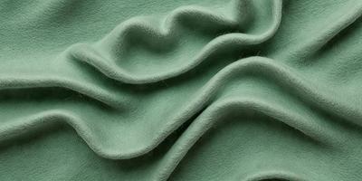The primary subject of the image is a green fabric, which appears to be a piece of wool. The setting is a close-up view of the fabric, showcasing its texture and color. The visual style is a realistic representation of the fabric, with no indication of digital art or illustration. The colors and mood of the image are predominantly green, giving it a natural and earthy feel.