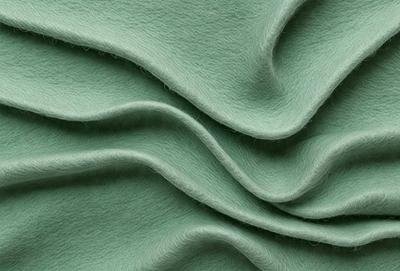 The primary subject of the image is a close-up of a green fabric, possibly a piece of wool or a textured material. The setting is a background of a similar green fabric, creating a visually cohesive scene. The visual style appears to be a close-up of the fabric, showcasing its texture and details. The colors and mood of the image are predominantly green, giving it a calm and soothing atmosphere.