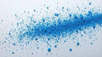 The primary subject of the image is a blue powder or substance, which appears to be a powdered blue dye or a blue pigment. The setting is a white background, which provides a clean and uncluttered environment for the blue powder to be the main focus. The visual style of the image is a close-up of the blue powder, showcasing its texture and color. The dominant colors in the image are blue and white, creating a calm and soothing atmosphere.