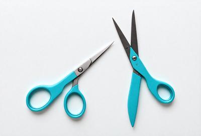 The primary subject of the image is a pair of blue scissors. The scissors are placed on a white surface, which serves as the setting or background. The visual style of the image is a photo, capturing the details of the scissors. The dominant colors in the image are blue and white, creating a clean and professional appearance.