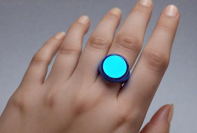 The primary subject of the image is a person's hand holding a blue ring with a blue light in the center. The setting is a white background, and the visual style appears to be a close-up of the hand and ring. The colors and mood of the image are predominantly blue, creating a calm and serene atmosphere.