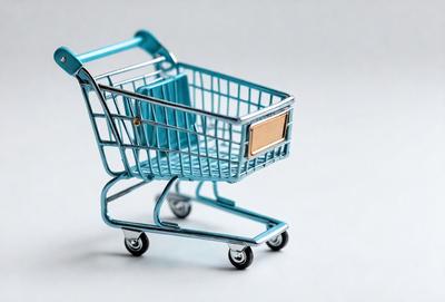 The primary subject of the image is a blue shopping cart. The cart is placed on a white surface, which serves as the setting or background. The visual style of the image is a photo, capturing the cart in its natural environment. The dominant colors in the image are blue and white, creating a clean and modern atmosphere.