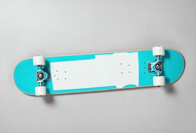 The primary subject of the image is a blue skateboard with white wheels. The skateboard is placed on a white surface, which serves as the background. The visual style of the image is a photo, capturing the skateboard in its natural environment. The dominant colors in the image are blue and white, creating a clean and modern appearance.