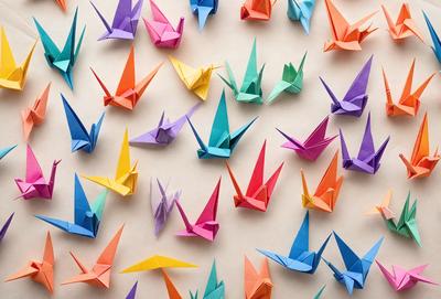 The primary subject of the image is a large collection of colorful origami cranes. The setting is a white background, and the visual style is a close-up of the origami cranes. The colors and mood of the image are vibrant and cheerful, with the cranes being the main focus of the scene.