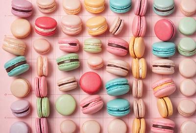 The primary subject of the image is a large collection of macarons, which are colorful and visually appealing. The macarons are arranged on a pink surface, which adds a touch of warmth and elegance to the scene. The visual style of the image is a close-up of the macarons, showcasing their intricate details and vibrant colors. The dominant colors in the image are pink, white, and various shades of green, blue, and yellow, creating a cheerful and