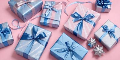 The primary subject of the image is a collection of six different colored gift boxes, each with a blue bow. The boxes are arranged on a pink surface, creating a visually appealing and festive display. The setting is a pink background, which complements the colors of the gift boxes. The visual style is a combination of photo and digital art, as the colors and details of the gift boxes are well-defined and realistic. The colors and mood of the image are predominantly pink and blue, creating a warm