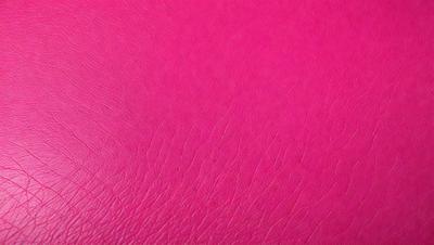 The primary subject of the image is a close-up of a pink leather surface. The setting is a pink background, which creates a visually striking contrast with the leather. The visual style is a photo, capturing the details and texture of the leather. The colors and mood of the image are predominantly pink, giving it a warm and inviting atmosphere.