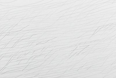 The primary subject of the image is a white background with a series of black lines or strokes. The setting appears to be a white wall, and the visual style is a combination of drawing and pattern. The black lines create a sense of depth and contrast against the white background, giving the image a somewhat moody and artistic atmosphere.