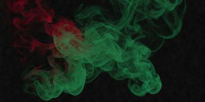 The primary subject of the image is a green and red smoke, which appears to be a digital art or illustration. The smoke is floating in a dark, possibly black, background. The visual style of the image suggests that it is a creative and artistic representation of the smoke, rather than a photo or a real-life scene. The colors and mood of the image are dominated by the green and red hues, which evoke a sense of energy and movement.