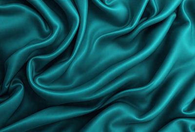 The primary subject of the image is a close-up of a blue fabric, possibly a piece of silk or velvet. The setting is a dark background, which contrasts with the vibrant blue fabric. The visual style appears to be a photo, as the fabric is captured in detail. The colors and mood of the image are predominantly blue, creating a calm and serene atmosphere.