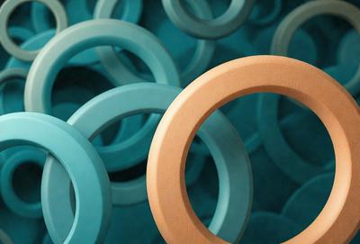 The primary subject of the image is a large, round, orange rubber ring. The ring is placed in the center of the image, surrounded by a variety of smaller, round rubber rings in different colors. The setting is a blue background, which contrasts with the vibrant colors of the rubber rings. The visual style is a close-up of the orange rubber ring, emphasizing its size and texture. The colors and mood of the image are lively and energetic, with the bright colors of the rub