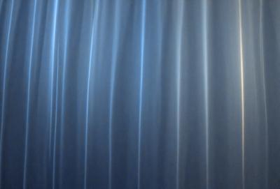 The primary subject of the image is a curtain, which is hanging in front of a blue background. The curtain appears to be made of fabric, and it is the main focus of the image. The setting is a stage or a theater, as the curtain is likely used to cover the stage when not in use. The visual style of the image is a close-up of the curtain, showcasing its texture and details. The colors in the image are predominantly blue, creating a calm and serene atmosphere