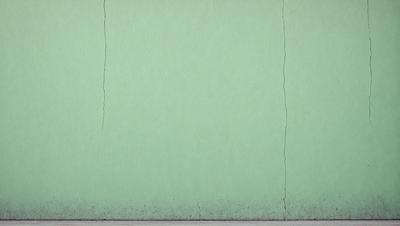 The primary subject of the image is a green wall with a crack in it. The setting is a room with a green wall, and the visual style is a photo. The dominant colors are green and white, creating a calm and soothing atmosphere.