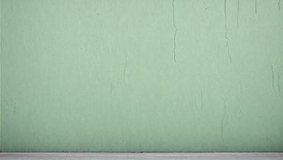 The primary subject of the image is a green wall with a peeling paint surface. The setting is a room with a green wall, and the visual style is a photo. The dominant colors are green and white, and the overall atmosphere is somewhat dull and aged due to the peeling paint.