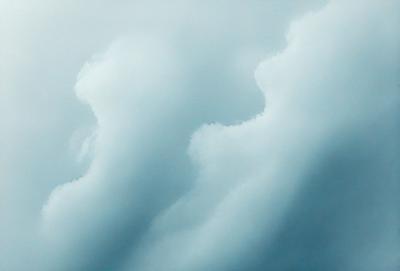 The primary subject of the image is a cloudy sky with two faces visible in the clouds. The setting is an outdoor environment, and the visual style appears to be a photo. The sky is predominantly blue, and the faces in the clouds give the scene a somewhat eerie or mysterious atmosphere.
