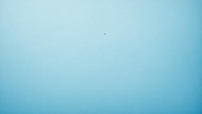 The primary subject of the image is a blue sky with a single dot in the middle of it. The sky appears to be cloudless, and the dot is the only visible object in the scene. The visual style of the image is a photo, and the colors and mood are predominantly blue, creating a calm and serene atmosphere.