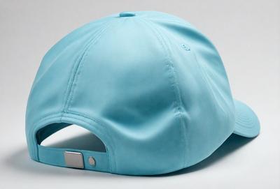 The primary subject of the image is a blue hat. The hat is placed on a white surface, which serves as the background. The visual style of the image is a photo, capturing the hat's details and colors. The hat has a blue color and a casual, sporty appearance.