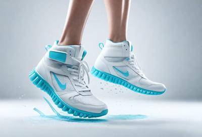 The primary subject of the image is a pair of white and blue Nike shoes. The shoes are floating in mid-air, with water droplets surrounding them. The setting appears to be a white background, which adds to the overall visual style of the image. The colors and mood of the image are predominantly blue and white, creating a clean and modern appearance.