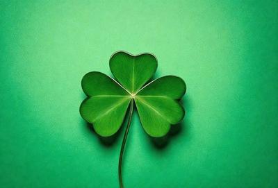 The primary subject of the image is a four-leaf clover, which is a symbol of good luck. The clover is placed on a green background, which adds to the overall atmosphere of the image. The visual style of the image is a close-up of the clover, showcasing its details and texture. The colors in the image are predominantly green, which is the color of the clover and the background.