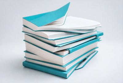 The primary subject of the image is a stack of books. The books are blue and white, and they are arranged in a pile. The setting is a white surface, which provides a clean and minimalist background for the books. The visual style is a close-up of the books, showcasing their colors and textures. The overall atmosphere is calm and organized, as the books are neatly stacked and well-presented.