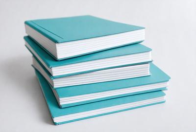 The primary subject of the image is a stack of books. The books are stacked on top of each other, and they are all blue in color. The setting is a white background, which provides a clean and minimalist appearance. The visual style is a photo, capturing the details of the books and their arrangement. The colors and mood of the image are predominantly blue, creating a calm and serene atmosphere.