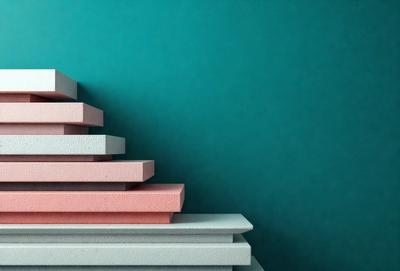 The primary subject of the image is a stack of books, which are pink and white in color. The books are arranged in a pyramid shape, with the top book being the largest and the bottom book being the smallest. The setting is a blue wall, which serves as the backdrop for the stack of books. The visual style of the image is a close-up, focusing on the details of the books and their arrangement. The colors and mood of the image are bright and cheerful, with the pink and white