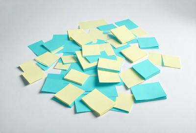 The primary subject of the image is a pile of yellow sticky notes. The setting is a white surface, which provides a clean and uncluttered backdrop for the sticky notes. The visual style is a close-up of the sticky notes, showcasing their details and textures. The colors and mood of the image are predominantly yellow and light, creating a warm and inviting atmosphere.