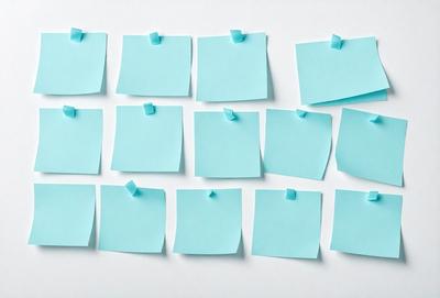 The primary subject of the image is a collection of blue sticky notes. These notes are attached to a white surface, possibly a wall or a table. The setting appears to be indoors, and the visual style is a close-up of the sticky notes. The overall atmosphere is calm and organized, as the blue notes are neatly arranged on the white surface.