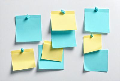 The primary subject of the image is a collection of yellow and blue sticky notes. These notes are attached to a white surface, possibly a wall or a table. The visual style of the image is a close-up of the sticky notes, showcasing their colors and text. The overall atmosphere of the image is bright and cheerful, as the yellow and blue notes create a lively and vibrant scene.