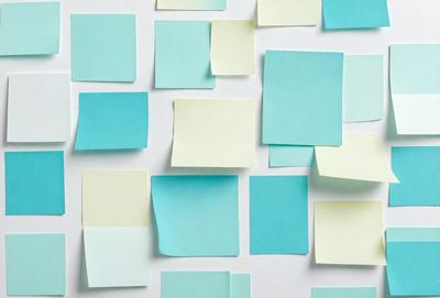 The primary subject of the image is a collection of yellow sticky notes. The setting is a white wall, and the visual style is a close-up of the sticky notes. The colors and mood of the image are predominantly yellow and light blue, creating a warm and inviting atmosphere.