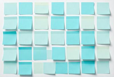 The primary subject of the image is a collection of blue post-it notes arranged in a square pattern on a white surface. The setting is a white wall, and the visual style is a close-up of the post-it notes. The colors and mood of the image are predominantly blue, creating a calm and organized atmosphere.