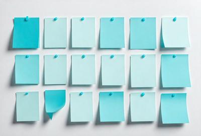 The primary subject of the image is a collection of blue sticky notes. These notes are attached to a white surface, which could be a wall or a table. The visual style of the image is a close-up of the sticky notes, showcasing their colors and textures. The overall atmosphere of the image is calm and organized, as the blue notes are neatly arranged on the white surface.