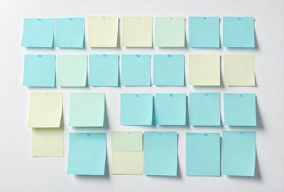 The primary subject of the image is a collection of yellow and blue sticky notes arranged on a white surface. The setting is a white wall, and the visual style appears to be a photo. The colors and mood of the image are predominantly blue and yellow, creating a warm and inviting atmosphere.